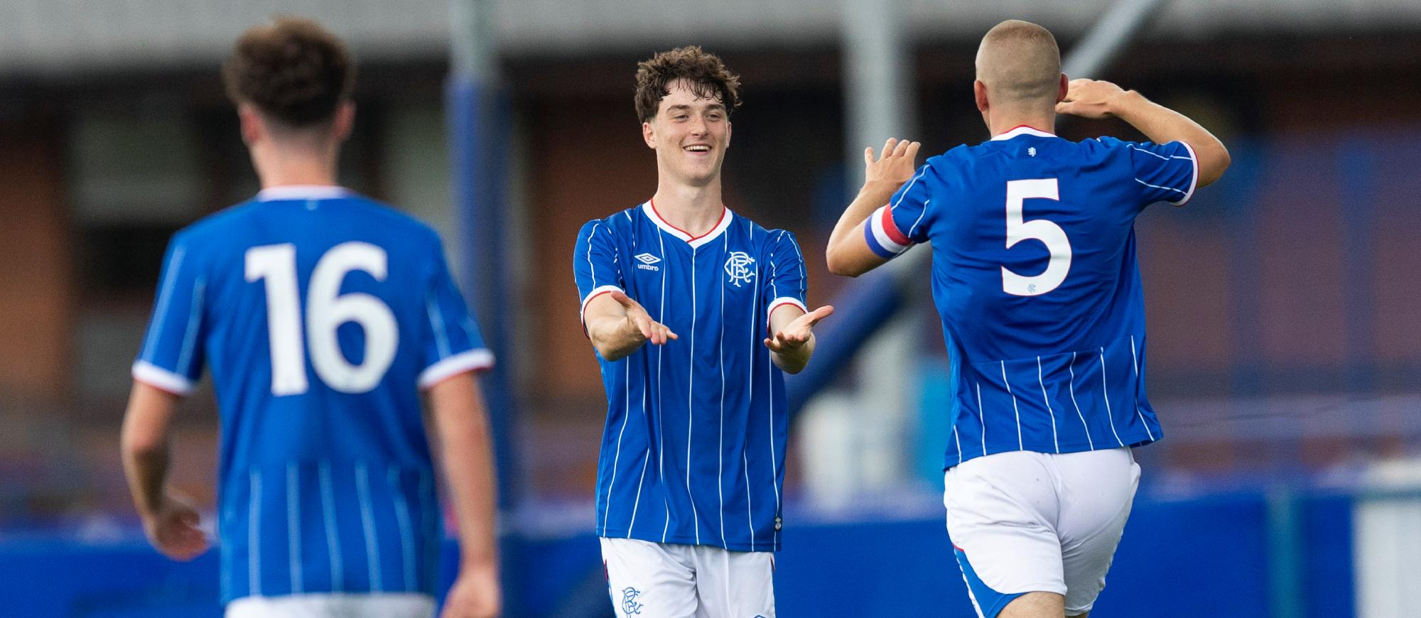 Three players in blue shirts, one with the number 5, celebrate on a football pitch.