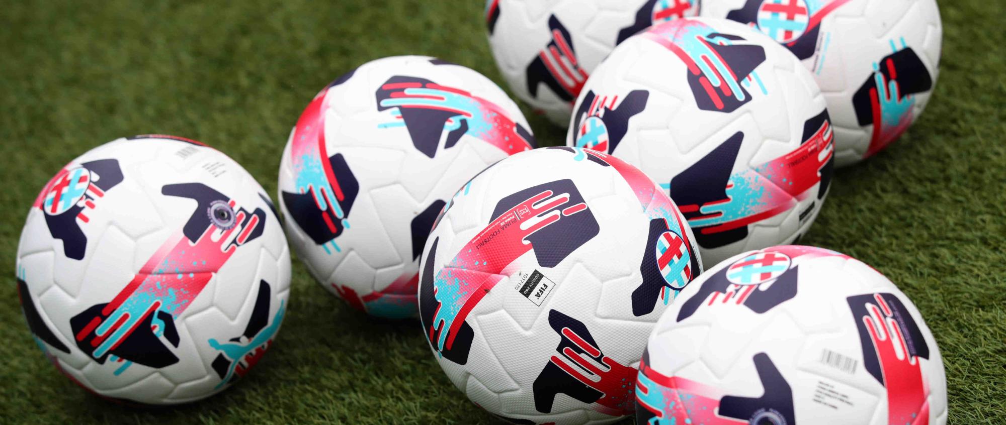 Seven footballs with pink, red and blue designs on green grass.