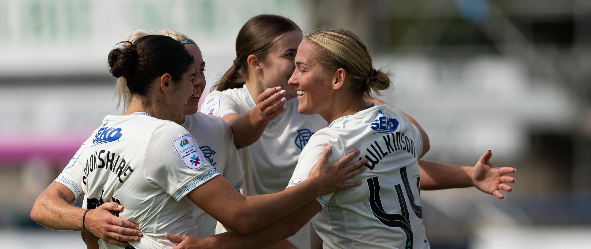 Four players in white jerseys celebrating a goal, one with "4" on the back.