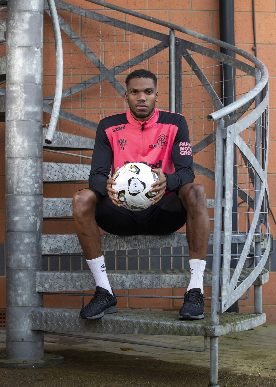 Football player in pink and black holding a ball on stairs