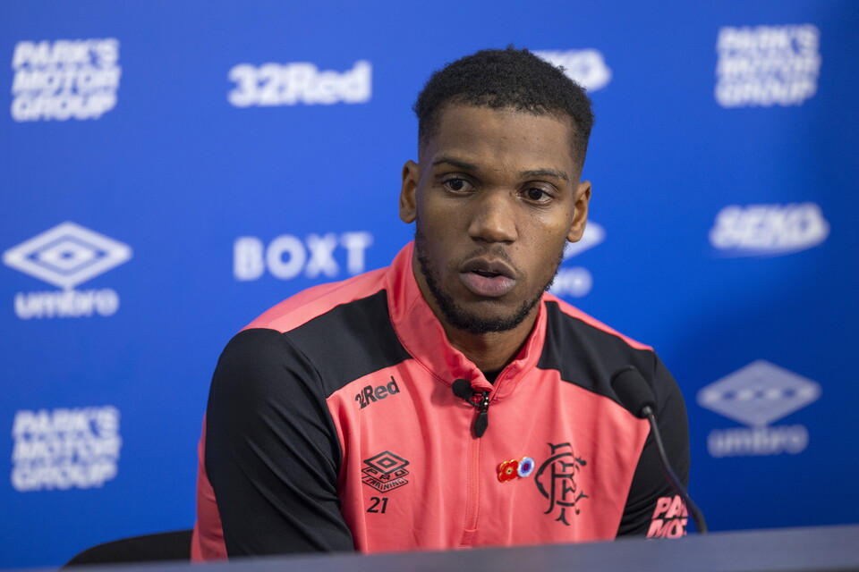 A footballer wearing a pink and black shirt speaks into a microphone.