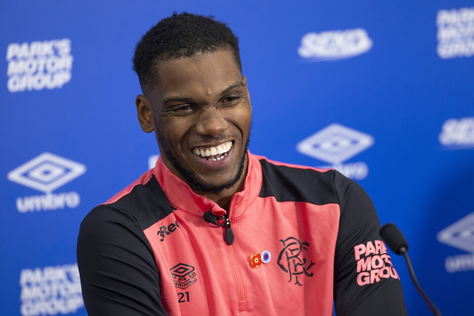 Footballer smiling at the camera wearing a pink and black shirt.