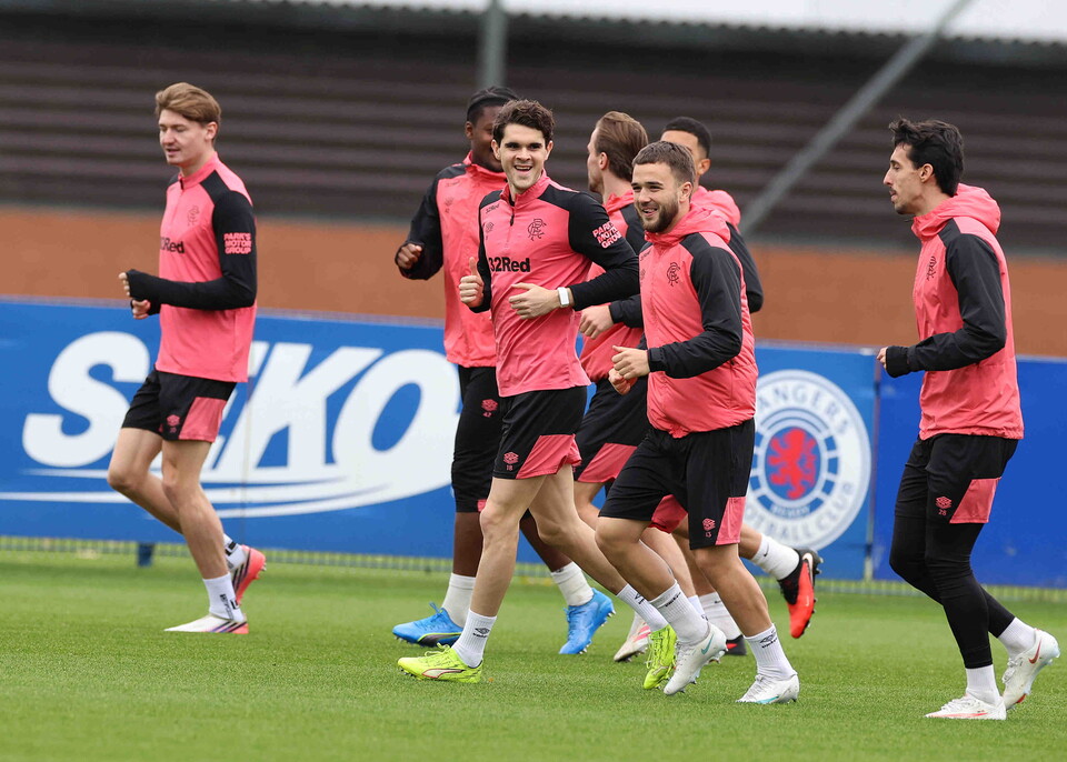 Six football players in pink and black training kits jog on a green pitch.