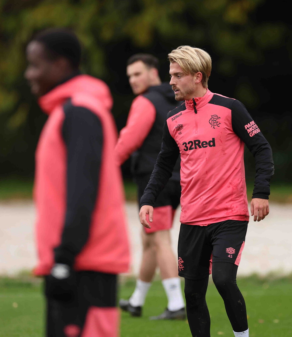 Three footballers wearing training gear on a football pitch, one in pink, another in black.