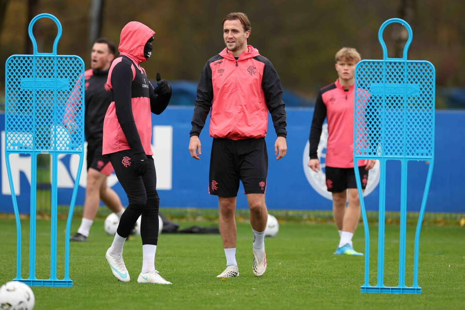Four players in pink jackets and black shorts run on a football pitch with blue goalposts.