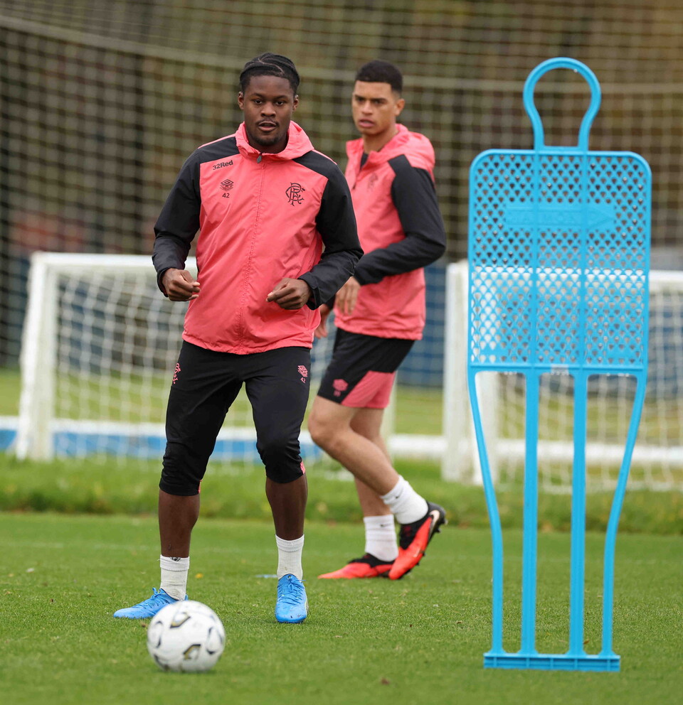 Two men in pink training kits kick a soccer ball on a field.