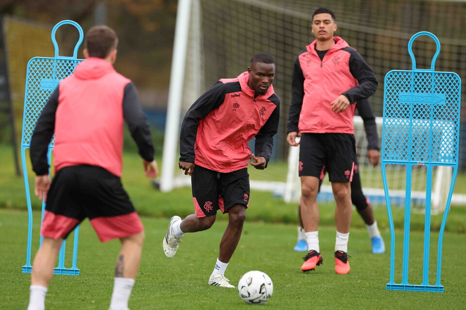 Three men in pink and black training gear run towards a soccer ball on a grass field.