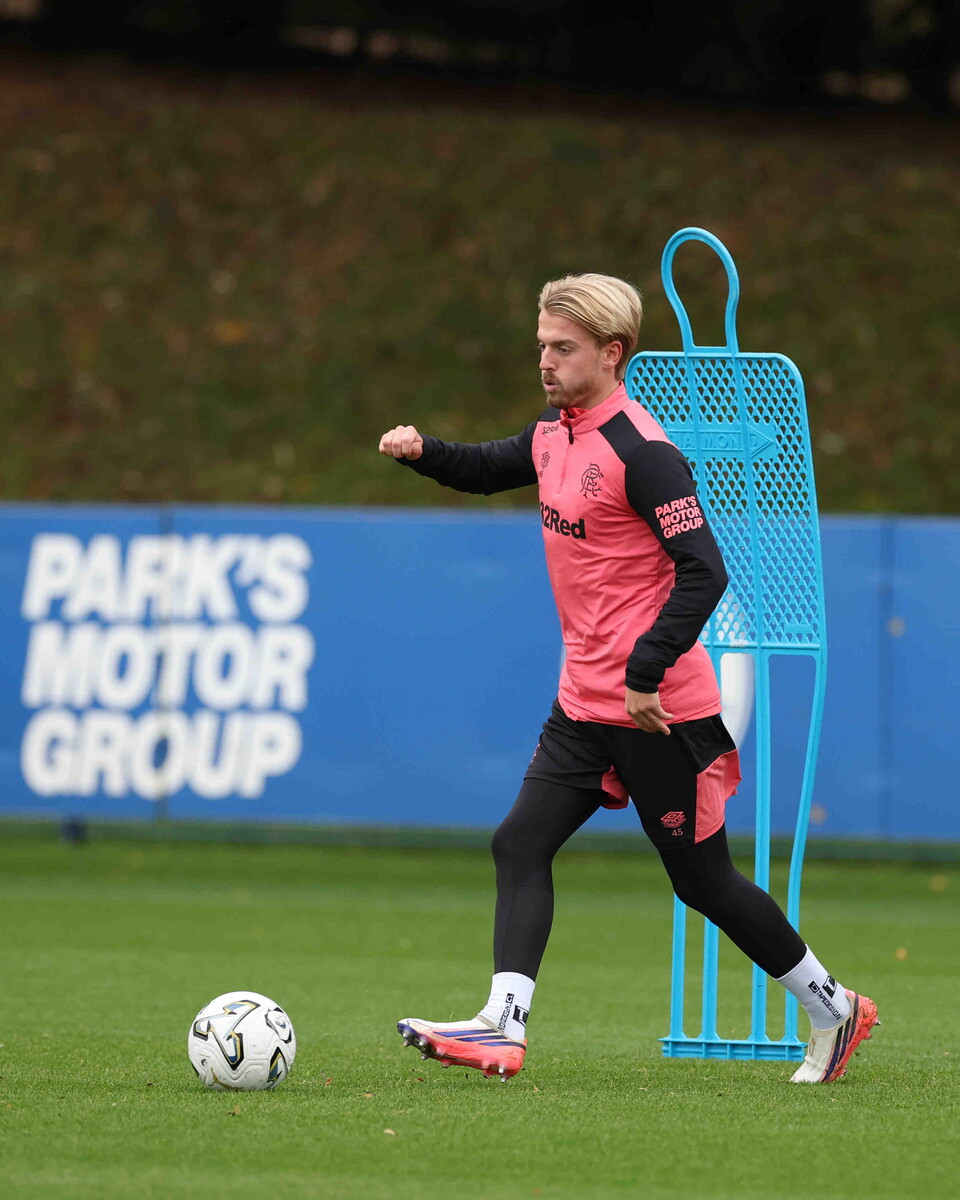 A footballer wearing a pink shirt and black leggings kicks a soccer ball on a grass pitch.