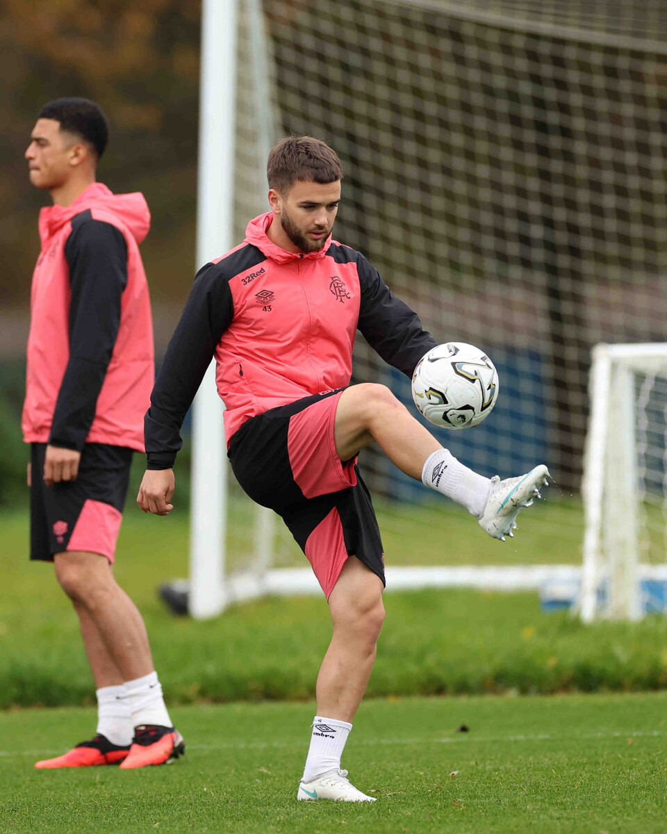A man in red and black football kit kicking a ball with another man in red and black kit behind him.