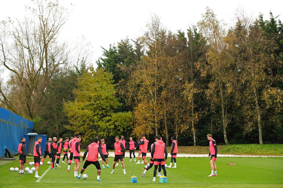 Players training in red and black shirts on a football pitch with trees in the background.
