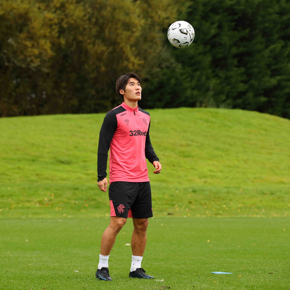 Man in pink and black shirt kicking football in air on green grass.