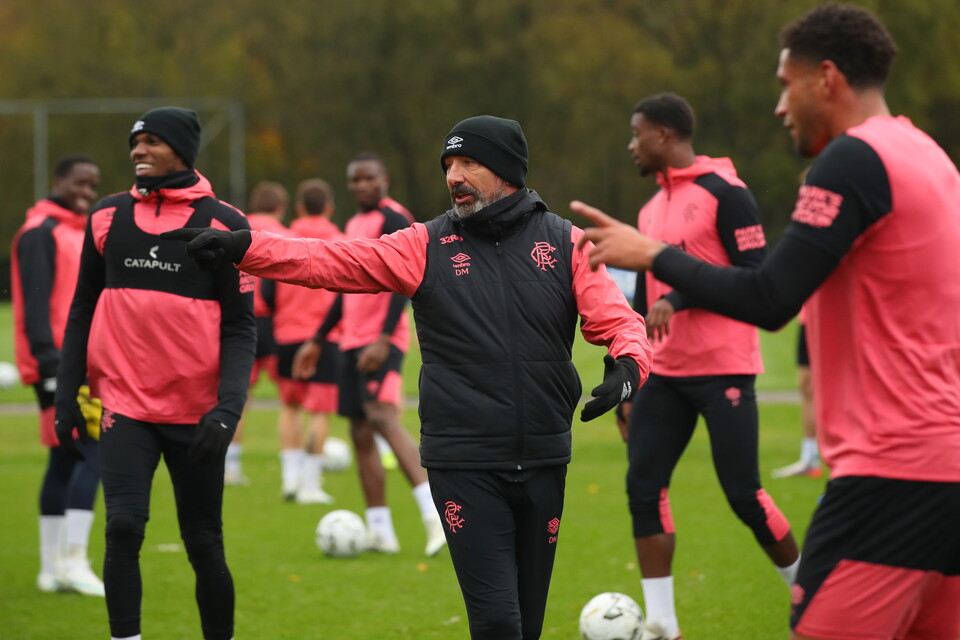 Football players in pink and black training kit with coach, one holding soccer ball
