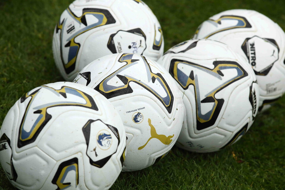 Six footballs with yellow, black and blue designs stacked on a grass pitch.