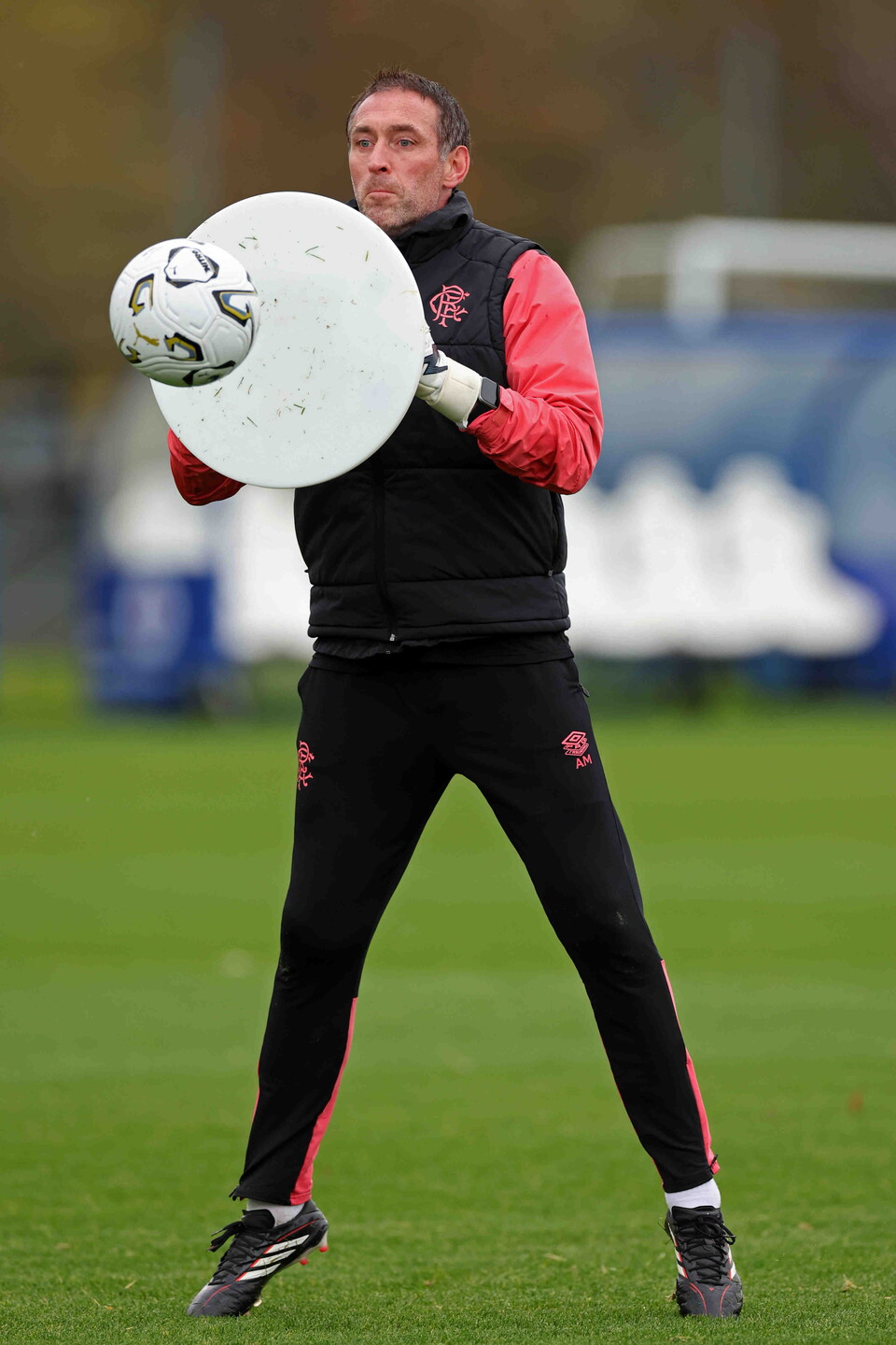 A football player catching a ball with a large pad on a football pitch.