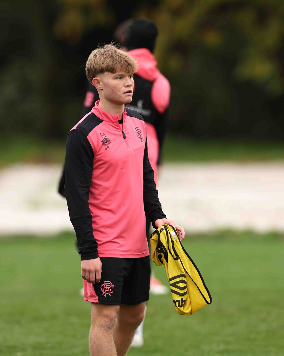 Football player in pink and black outfit holding yellow bag standing on grass field.