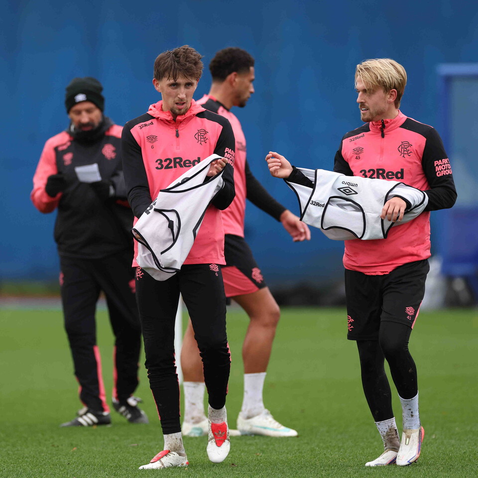Four football players in pink training suits walking on a pitch, holding bags.