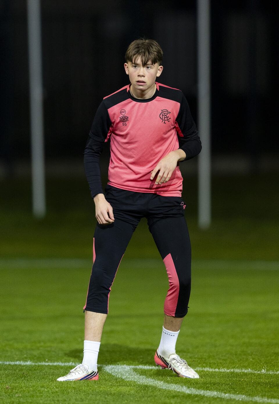 Football player in pink and black kit on field with pitch markings