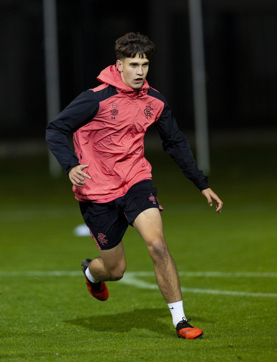 A male football player in a red jacket runs across the pitch.