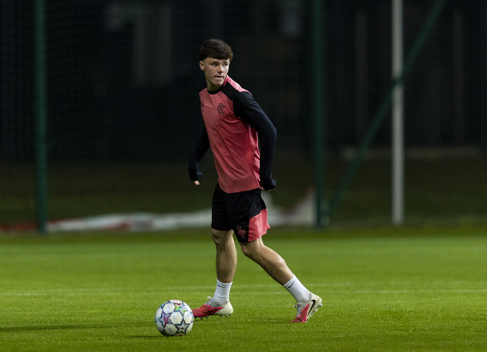A footballer in red and black, running towards a ball on a pitch.