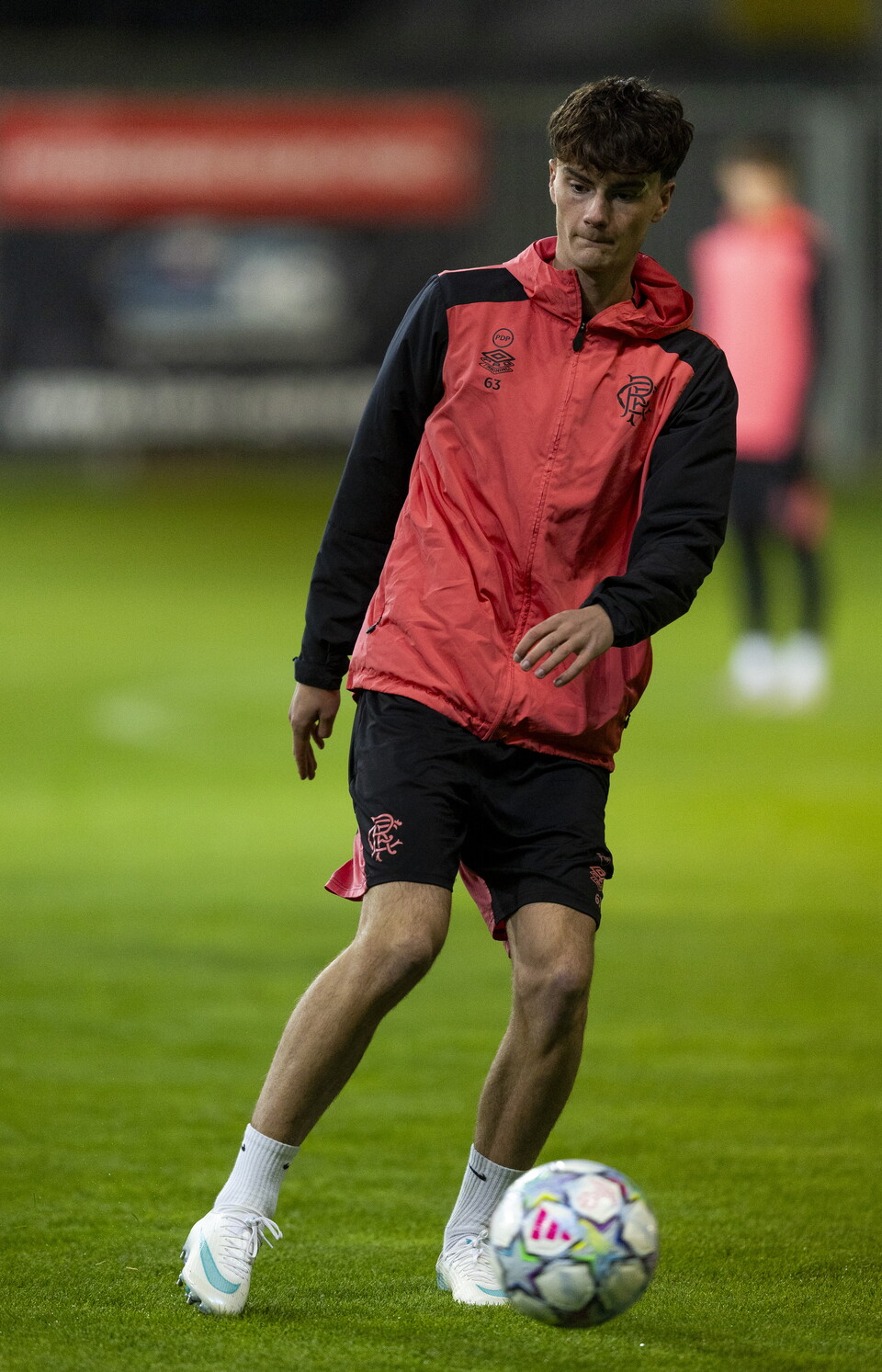 Football player in red and black kit kicking soccer ball on green pitch