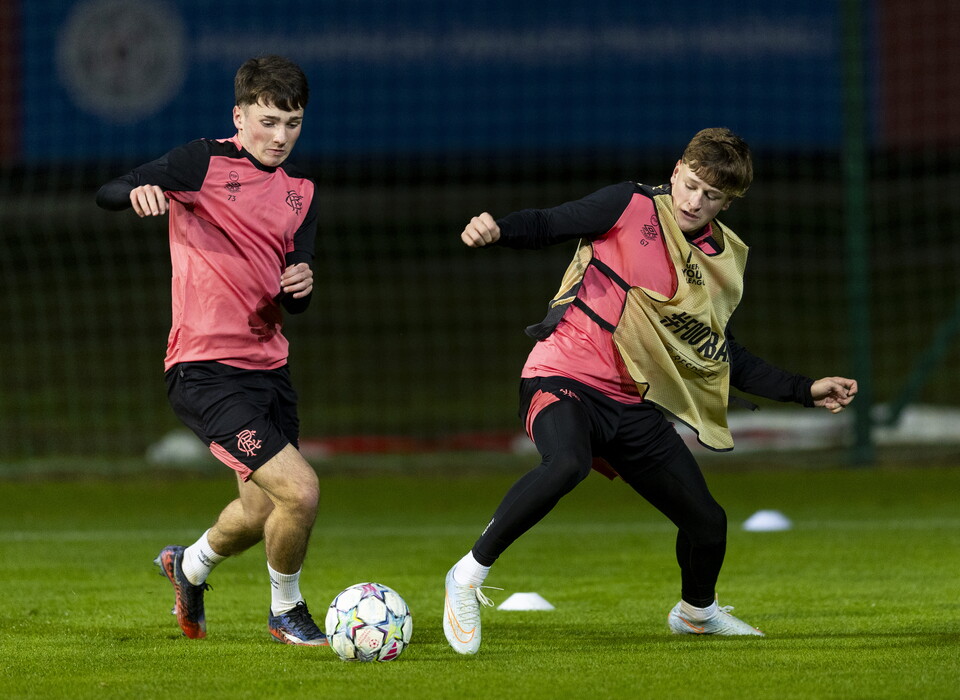 Two footballers, one in red and one in pink, chase a ball on a field.