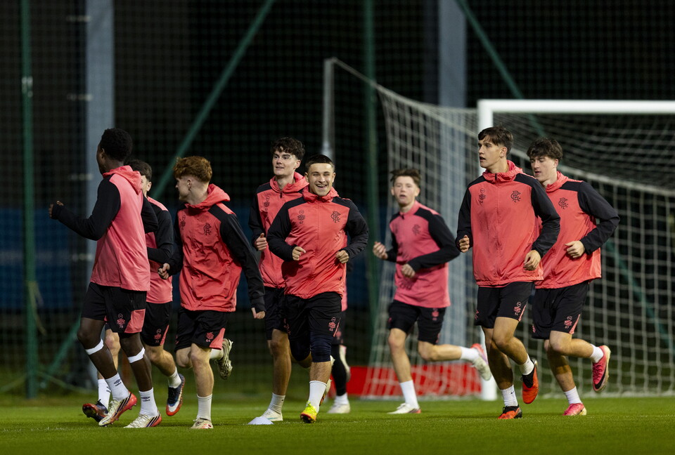 Soccer players in red and black shirts and shorts run across a football pitch.