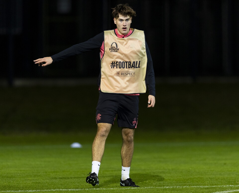 Football player in a tan vest stretches on the field at night.