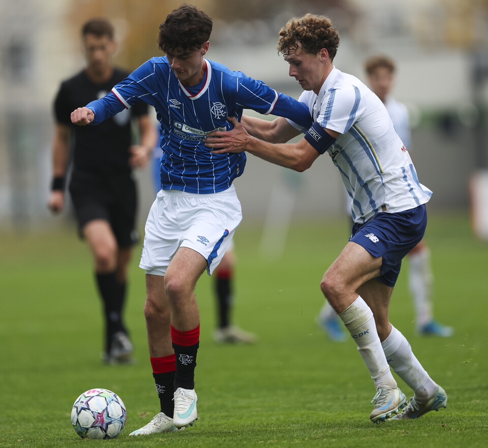 Two football players, one in blue and white, the other in white and blue, compete for the ball on a green field.
