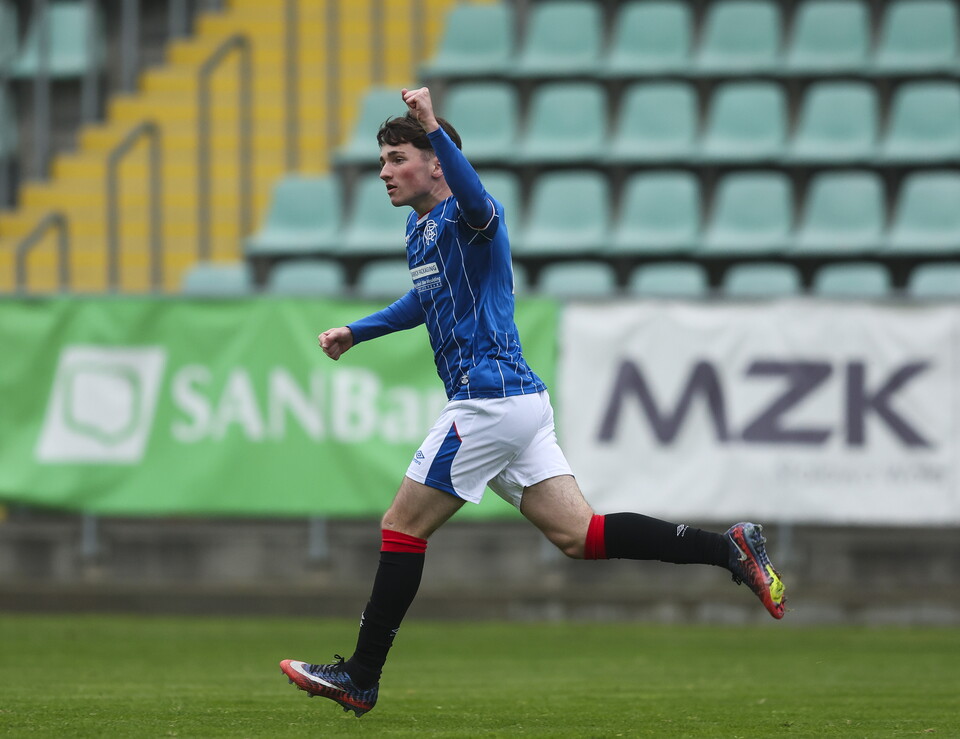 A footballer celebrates with his fist in the air on a football pitch with empty stands.