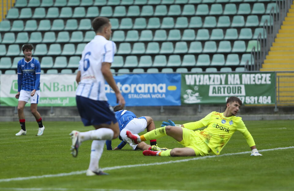 A football match with players in action on the field, one diving for a save.