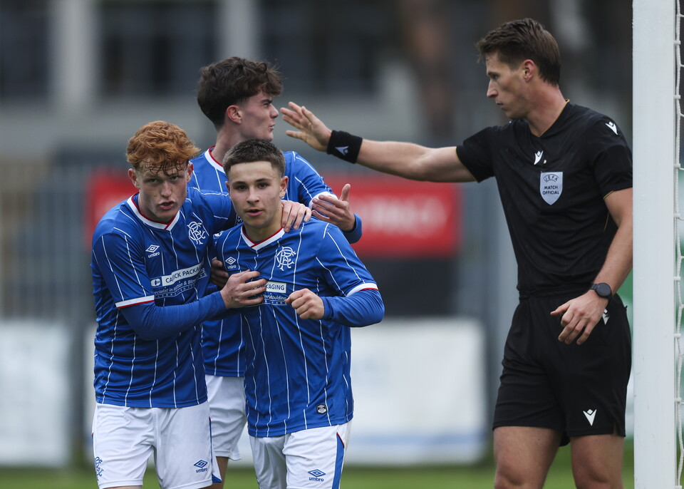Three players in blue jerseys celebrate near a referee in black.