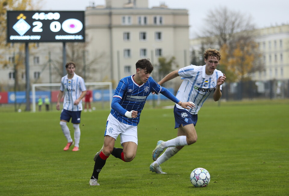 Players on a football field, one in blue shirt chasing the ball