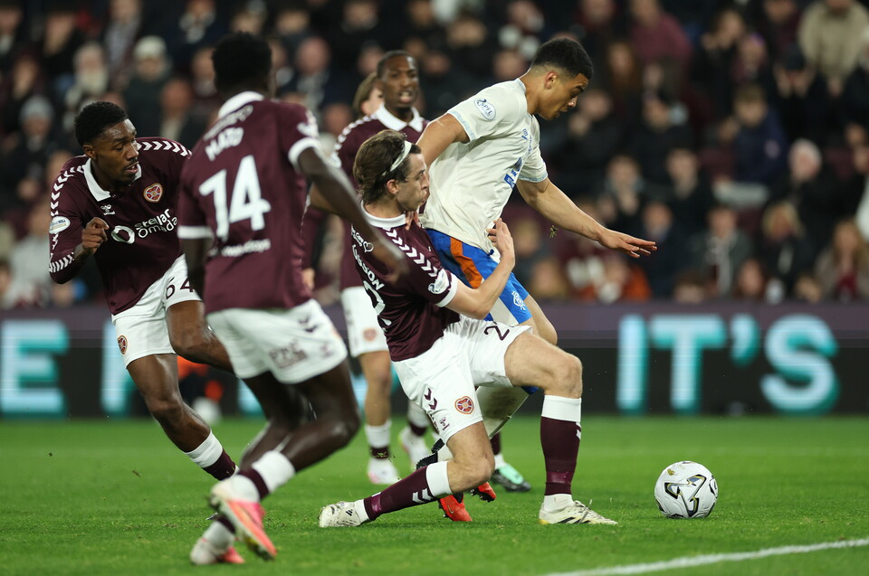 Football players in maroon and white uniforms compete for the ball on the pitch.