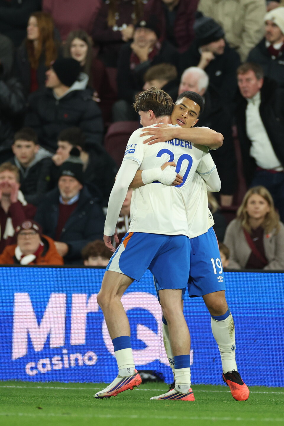 Two football players, one in white and blue, the other in blue, celebrating a goal.