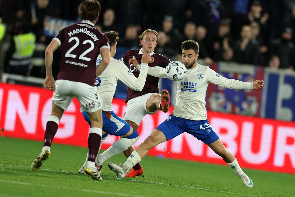 Players compete for ball, one wears white, others maroon, blue shorts, spectators watch.
