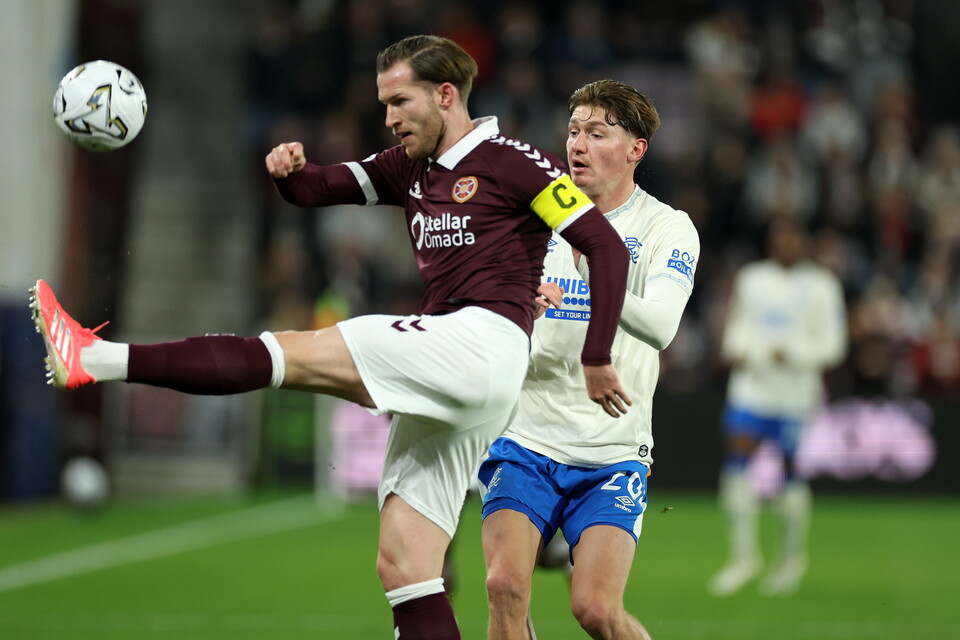 Footballer kicking ball in air during match, opponent in blue shorts nearby.