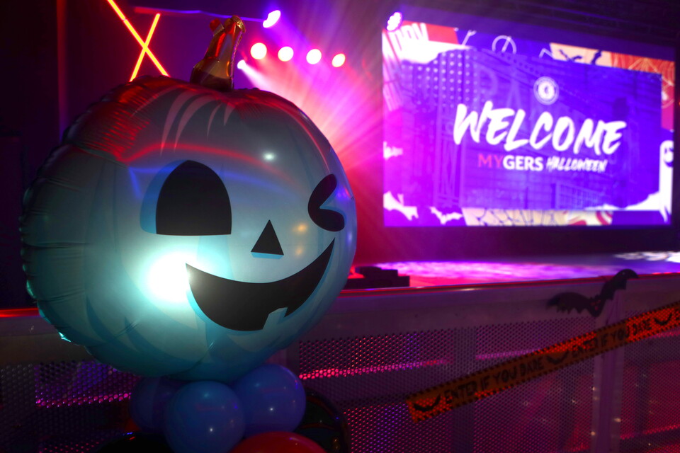 A large blue pumpkin balloon with a scary face stands in front of a lit stage.