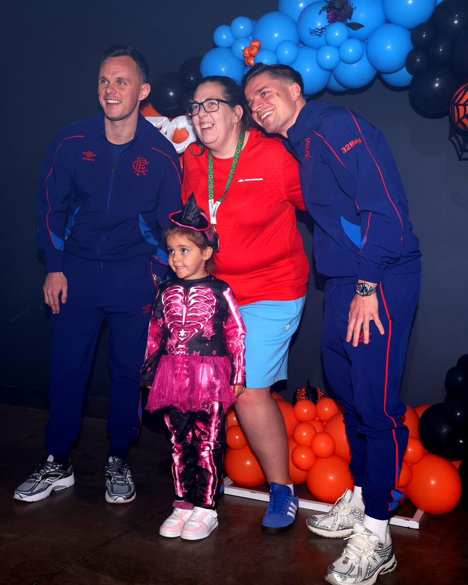 Three people and a child stand next to a wall of balloons, all wearing blue tracksuits.