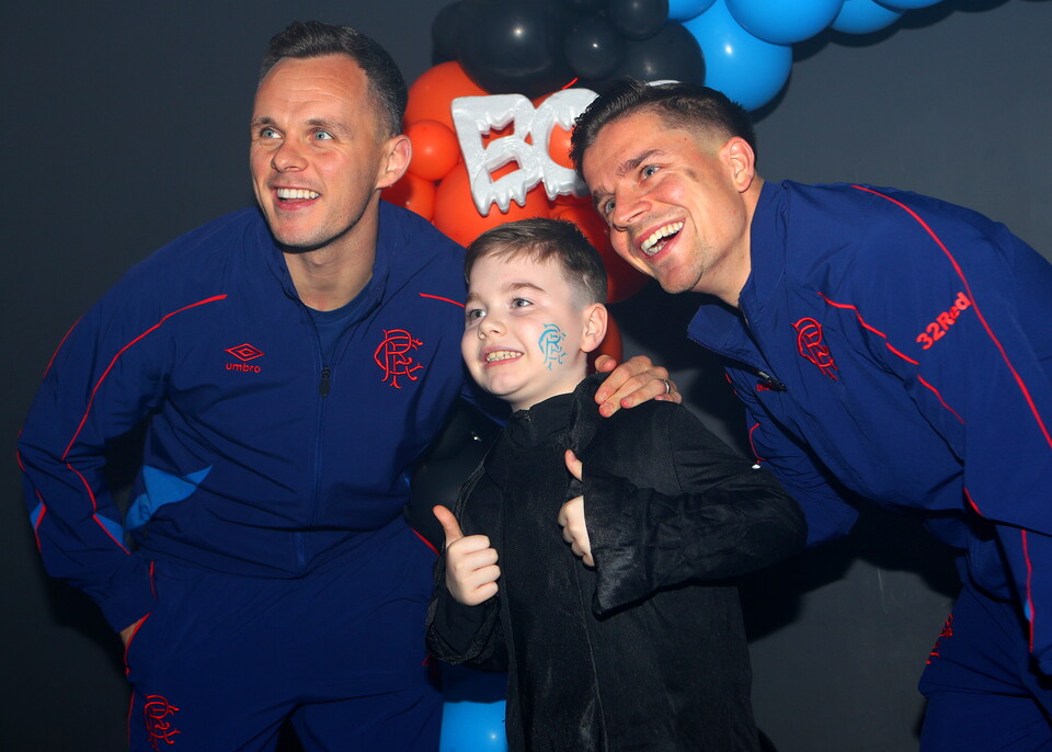 Three men in blue tracksuits with a child, all smiling at a celebration.