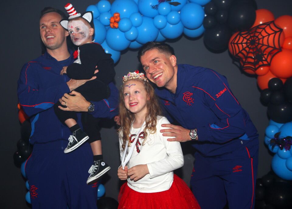 Two men and two children in matching blue suits pose for a photo in front of a Halloween balloon backdrop.