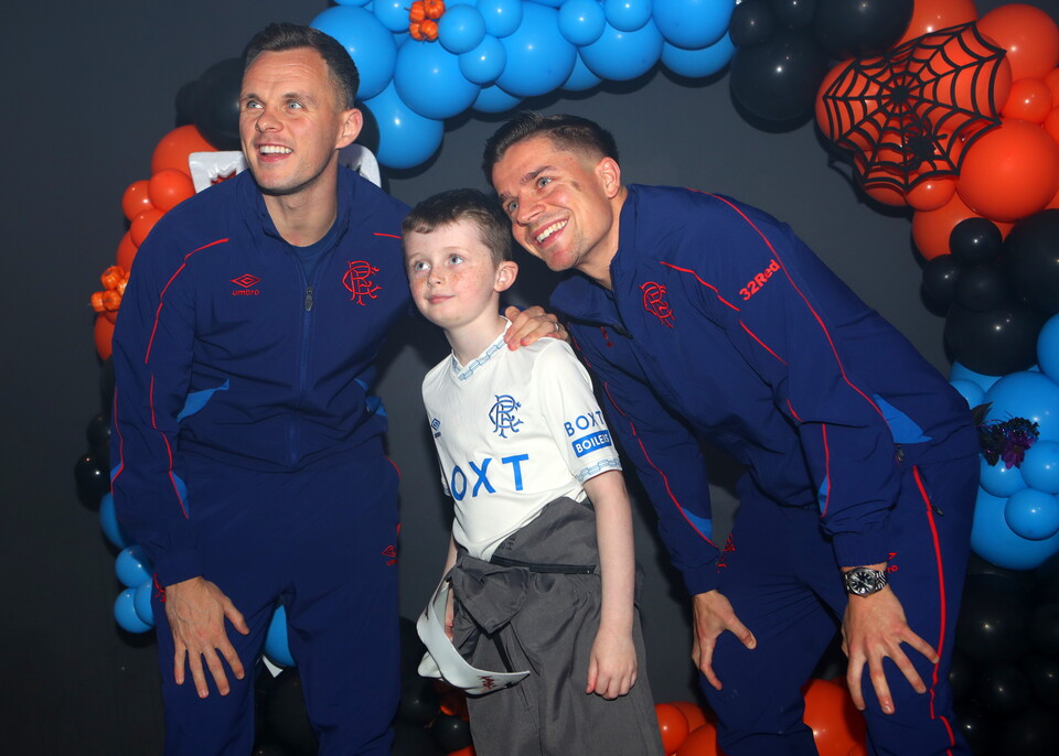 Three football players pose with a young fan in front of Halloween decorations.