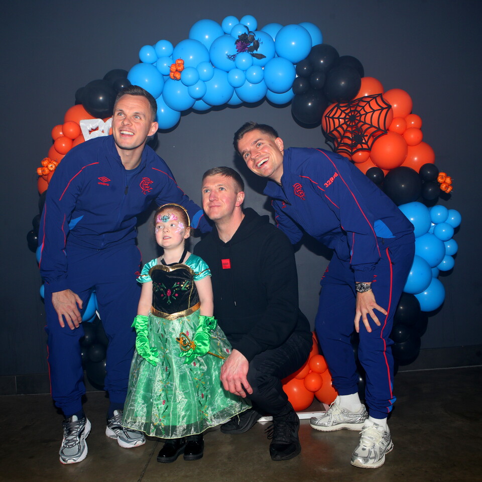 Three men and a girl pose in front of a balloon arch