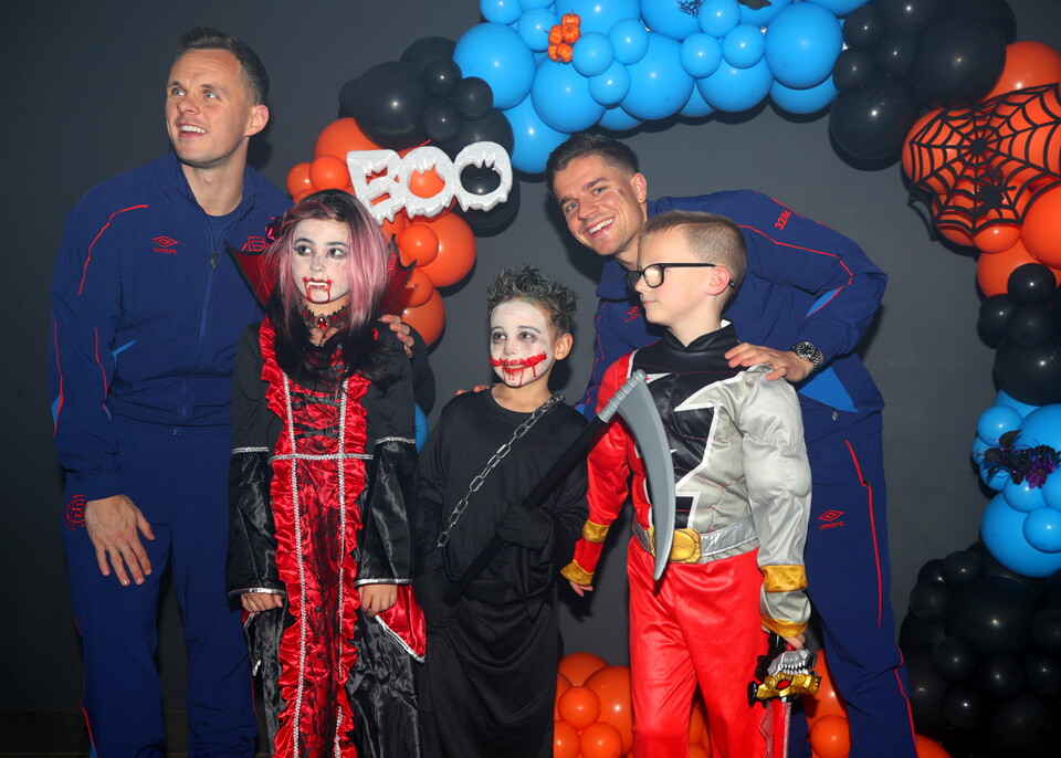 Five people in costumes in front of balloons with a spider web