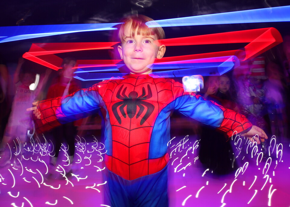 Boy in red Spider-Man costume standing in a dark room with glowing lights.