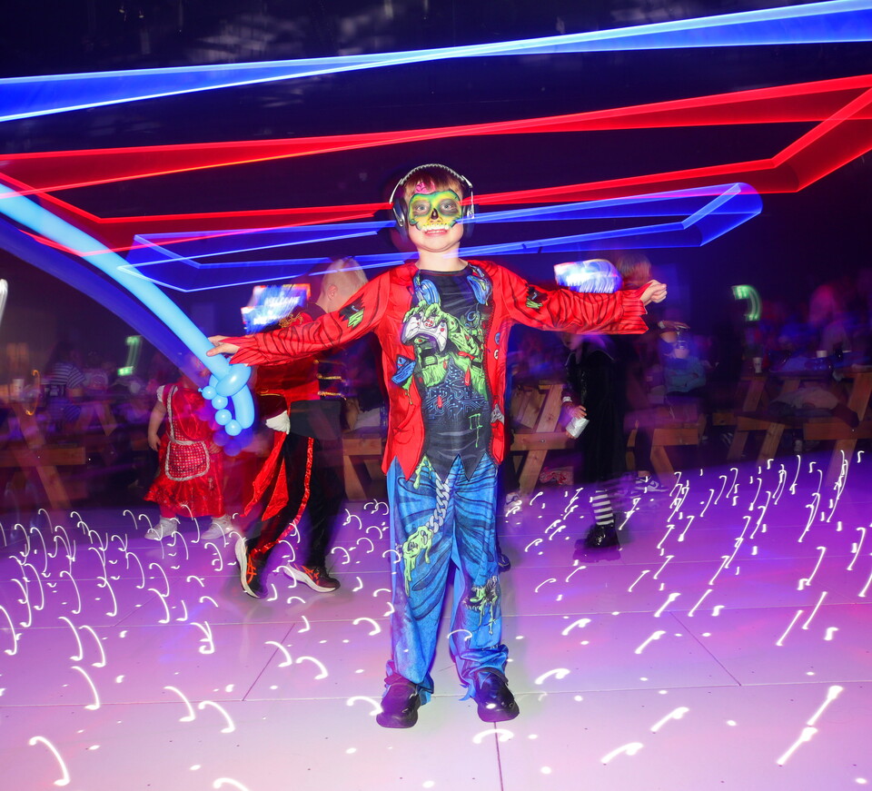 Child wearing a costume holds a sword on a dance floor with colourful lights.
