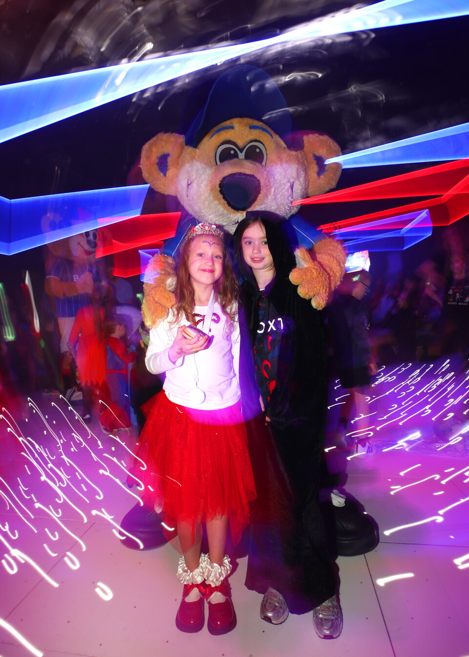 Two children stand on a dance floor with a large bear mascot.