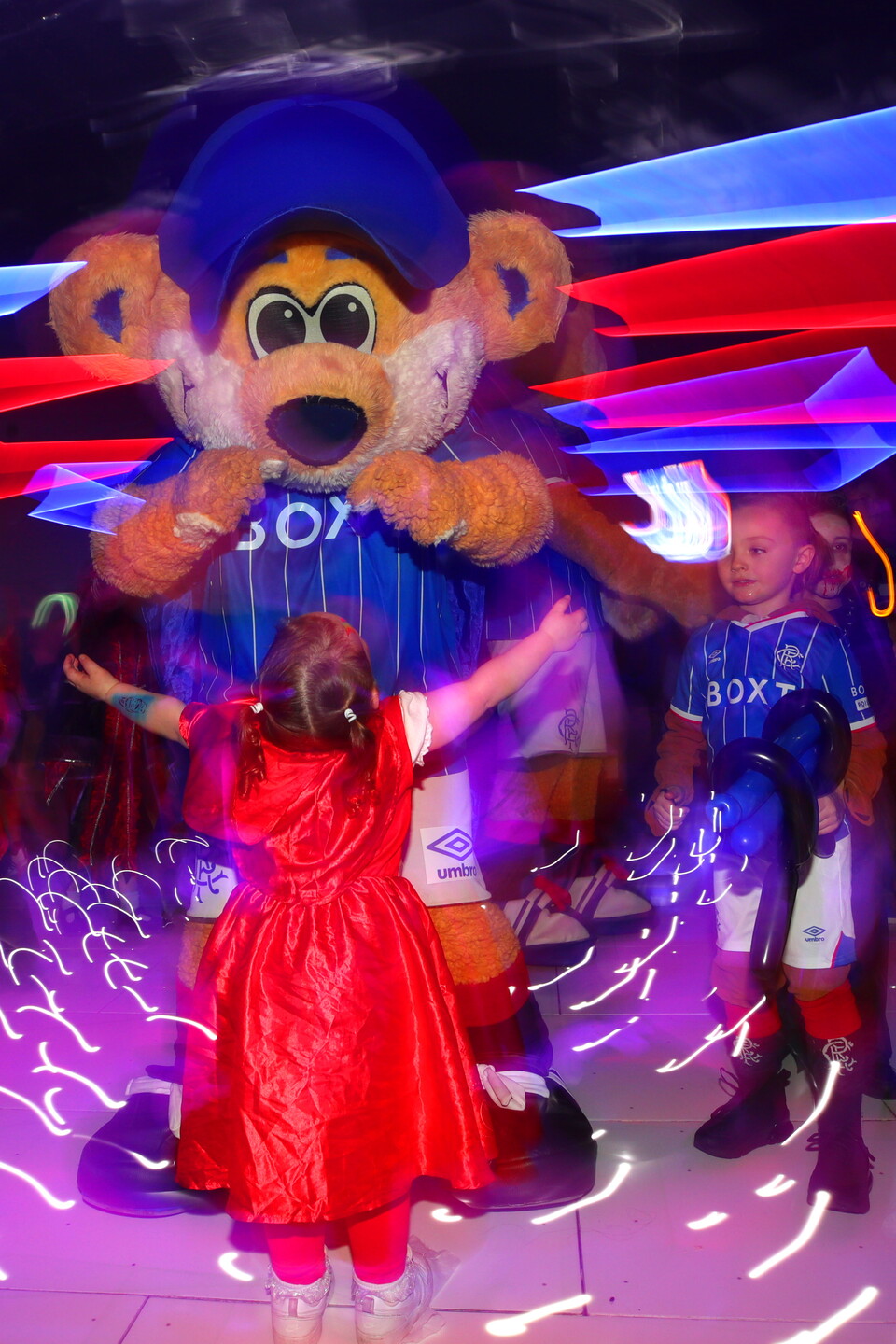 Child dancing with mascot in blue and red shirt in brightly lit room