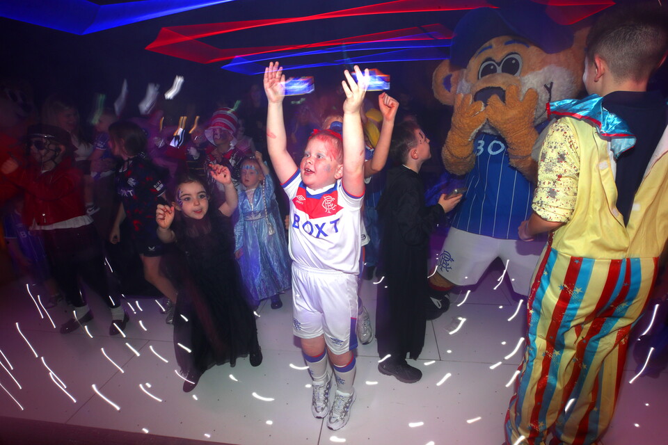 A young footballer celebrates at a Halloween party with a mascot and others in costumes.