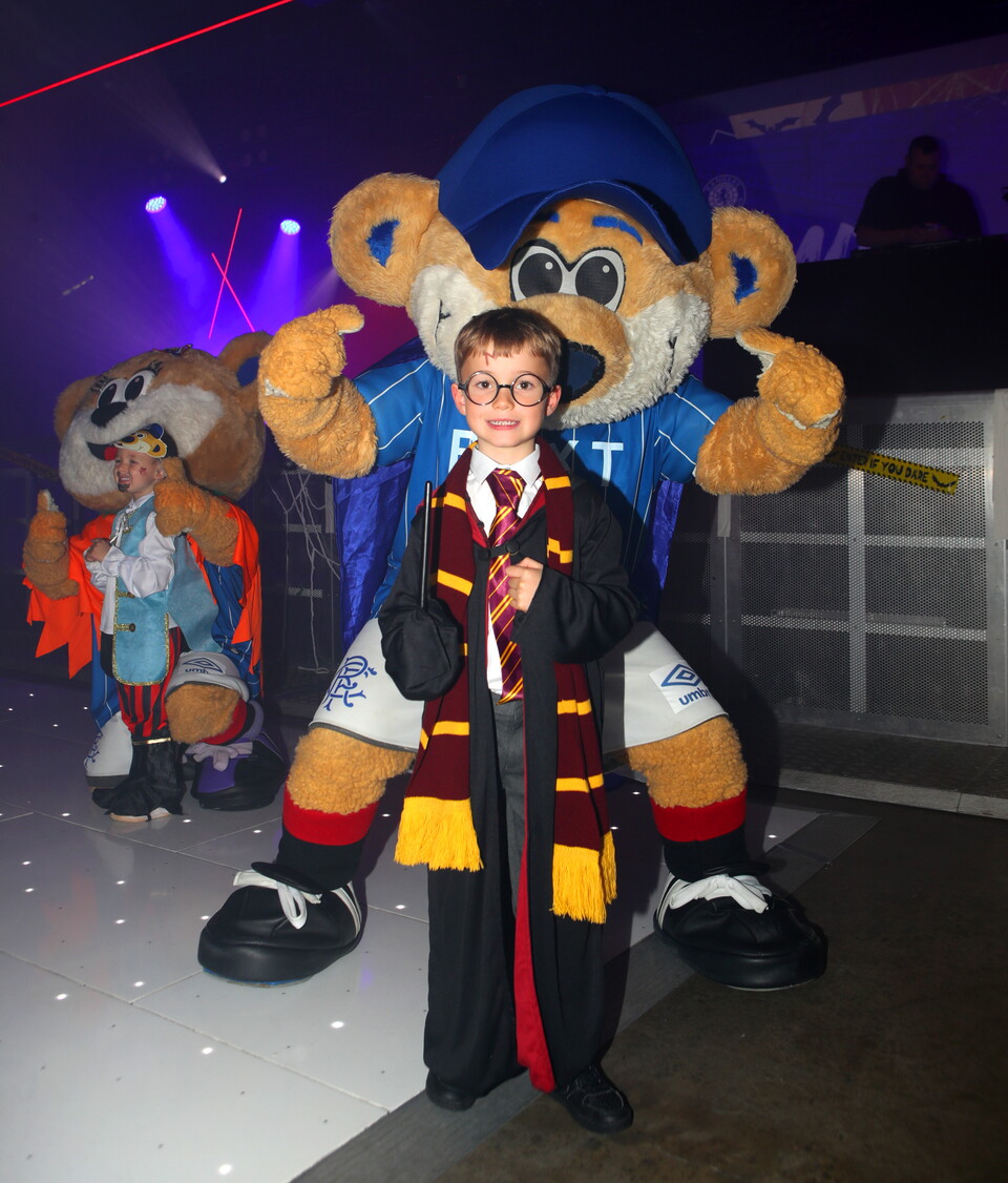 A young boy stands in front of mascots at a special event