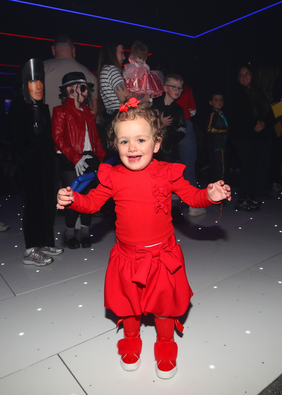 A young girl in a red costume with a red bow smiles at the camera.